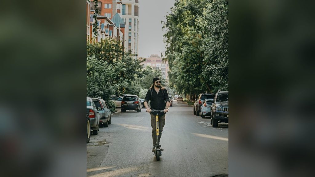 Bearded man riding an electric kick scooter on a street