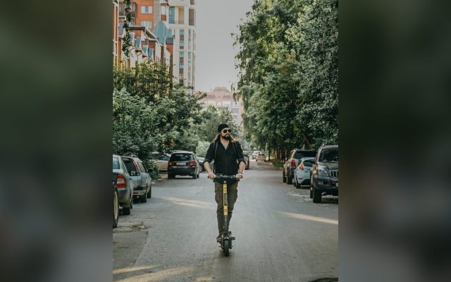 Bearded man riding an electric kick scooter on a street