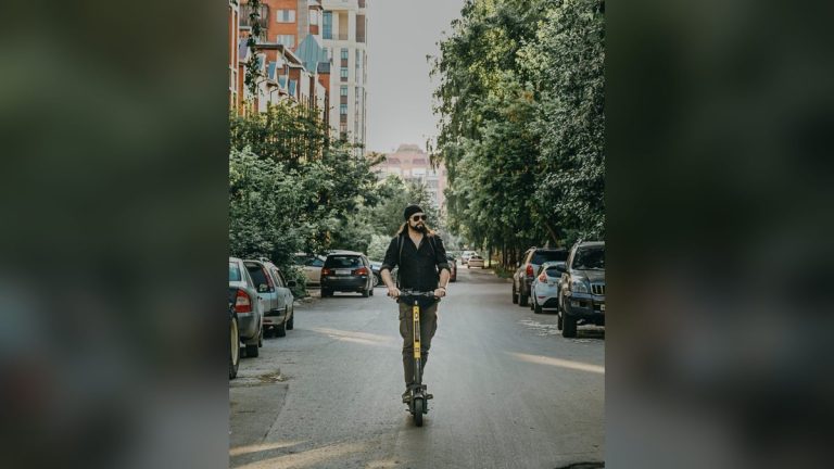 Bearded man riding an electric kick scooter on a street