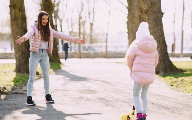Child riding a kick scooter with her mother