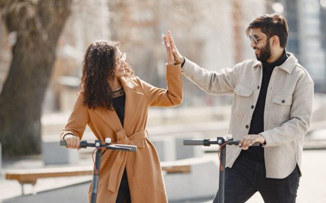 Couple high-fiving while riding electric scooters
