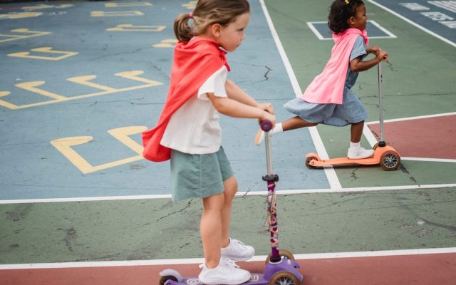 Girls in capes racing kick scooters on a playground