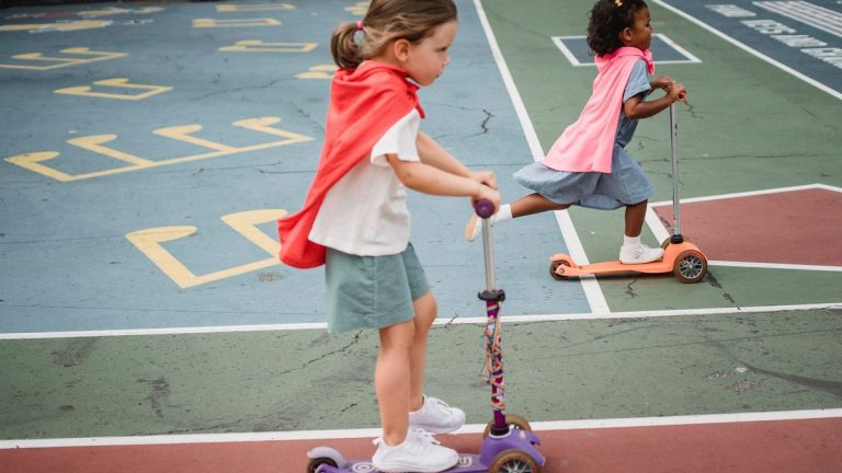 Girls in capes racing kick scooters on a playground