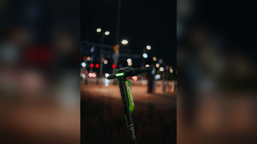 Green electric scooter with its light on at night
