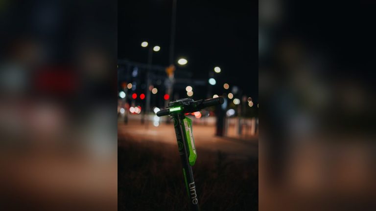 Green electric scooter with its light on at night