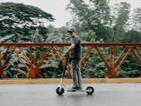 Man riding a shared electric scooter across a leafy bridge