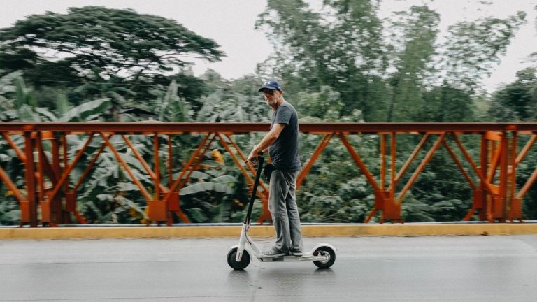 Man riding a shared electric scooter across a leafy bridge