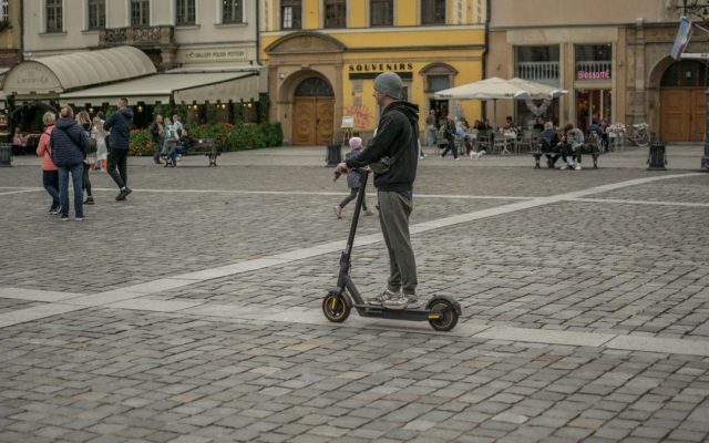 Man riding an e-scooter through a historic city square