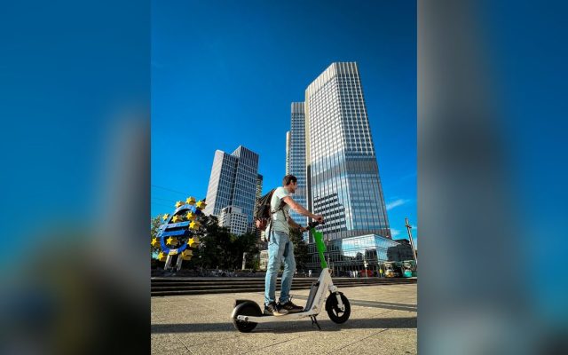 Man riding an electric scooter in front of city skyscrapers