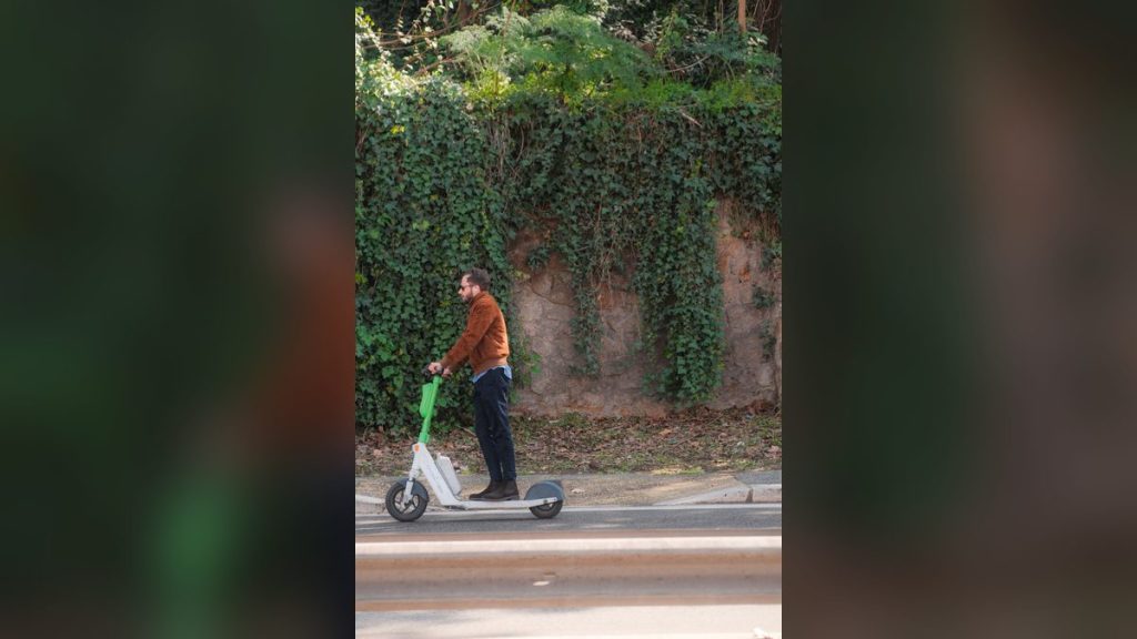 Man riding an electric scooter past an ivy-covered wall