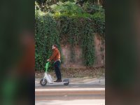 Man riding an electric scooter past an ivy-covered wall