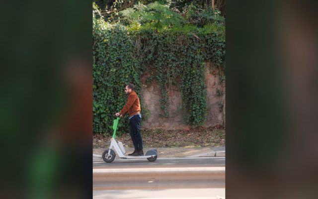Man riding an electric scooter past an ivy-covered wall