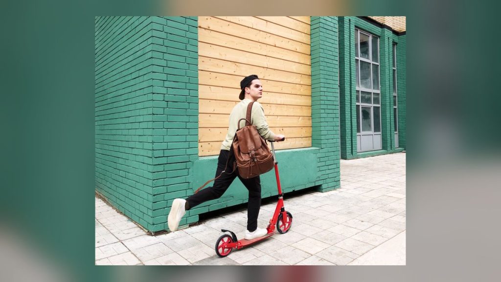 Man with a backpack on a red kick scooter in the city