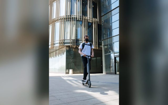 Man with backpack riding an e-scooter near a modern building