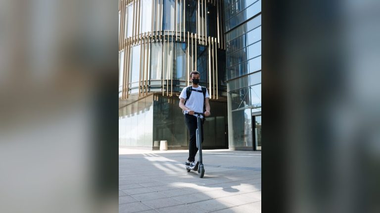 Man with backpack riding an e-scooter near a modern building