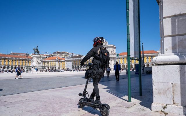 Rider on an electric scooter crossing a sunny city plaza