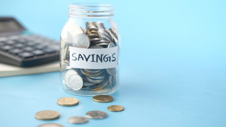 Savings jar filled with coins beside a calculator