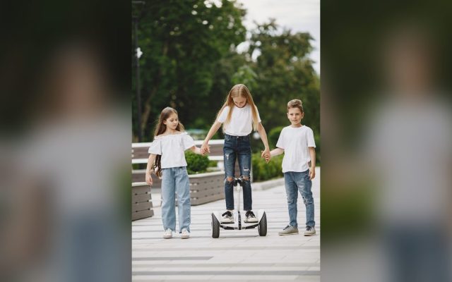 Three children playing with a self-balancing scooter in a park