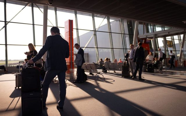 Travellers in a busy airport terminal with carry-on luggage