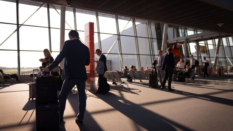Travellers in a busy airport terminal with carry-on luggage