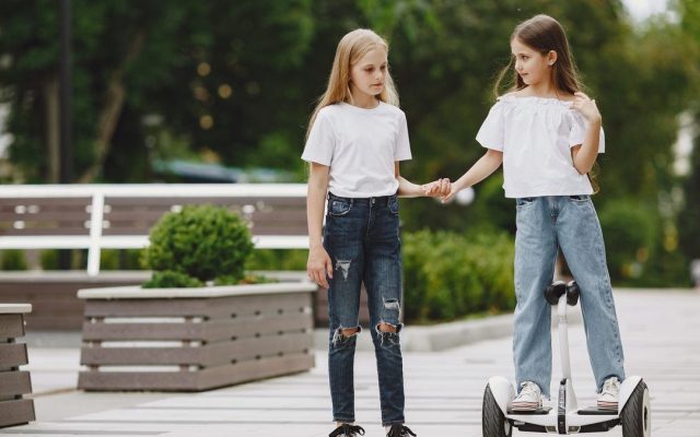 Two girls holding hands, one riding a self-balancing scooter