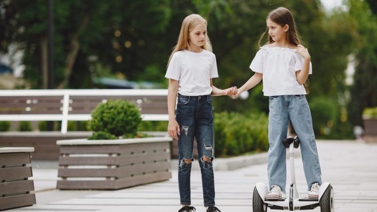Two girls holding hands, one riding a self-balancing scooter