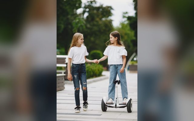 Two girls, one riding a kids' electric scooter