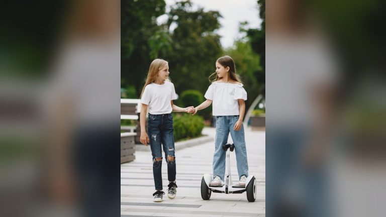 Two girls, one riding a kids' electric scooter