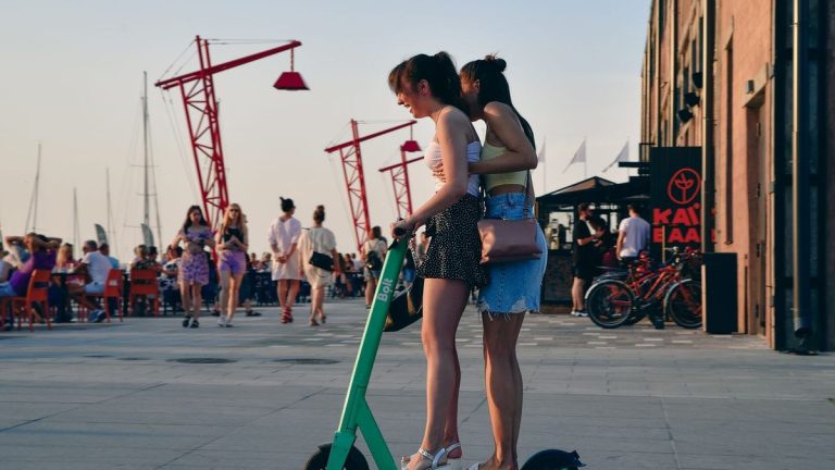 Two young women with an electric scooter at the waterfront