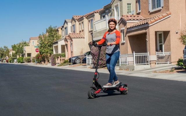 Woman riding a dual-motor electric scooter on a suburban street