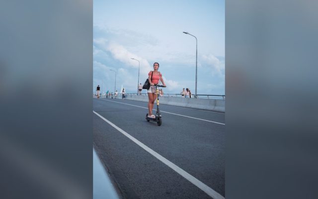 Woman riding an electric scooter across a city bridge