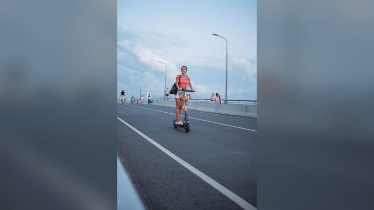 Woman riding an electric scooter across a city bridge