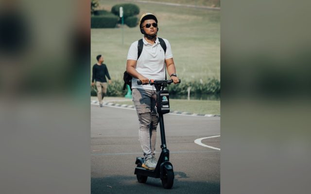 Young man in a helmet riding an electric scooter in a park