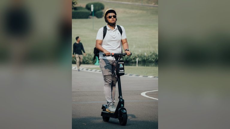 Young man in a helmet riding an electric scooter in a park