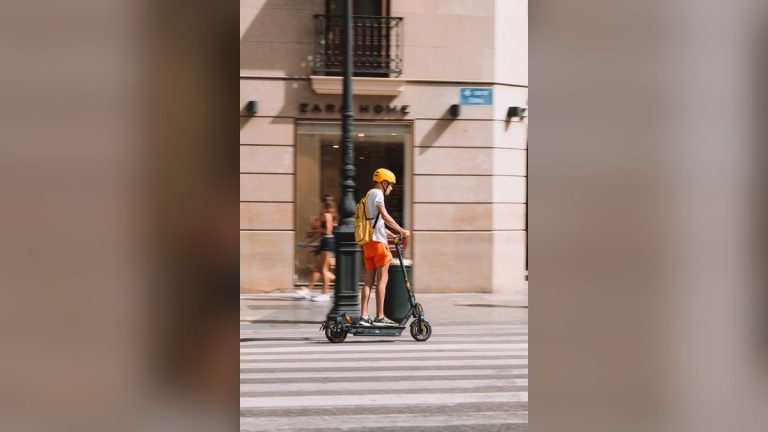 Young man in a helmet riding an electric scooter on a city street