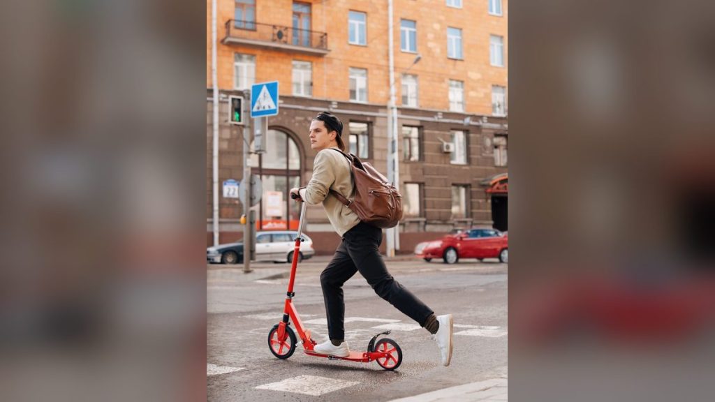 Young man riding a kick scooter on a city street