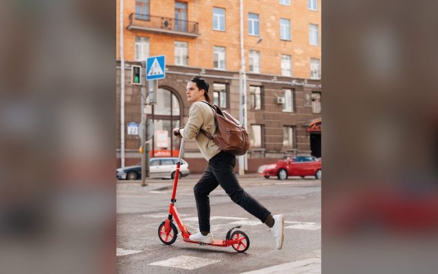 Young man riding a kick scooter on a city street
