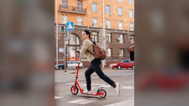 Young man riding a kick scooter on a city street