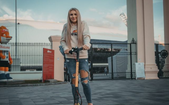 Young woman riding an electric scooter near a stadium