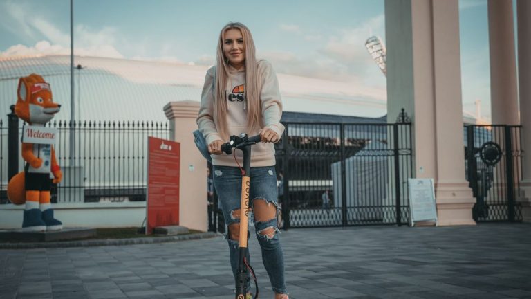 Young woman riding an electric scooter near a stadium