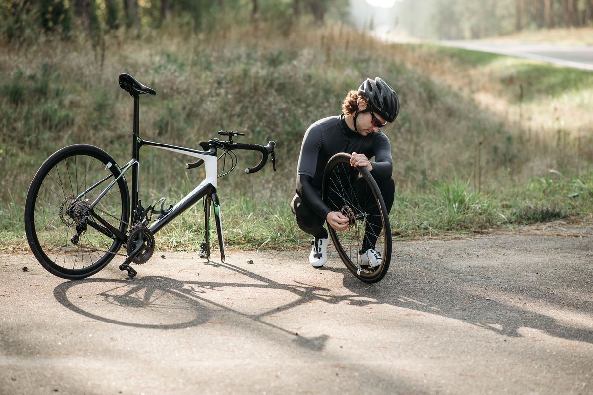 A cyclist in a helmet repairs a tire on a road bike in a serene country setting