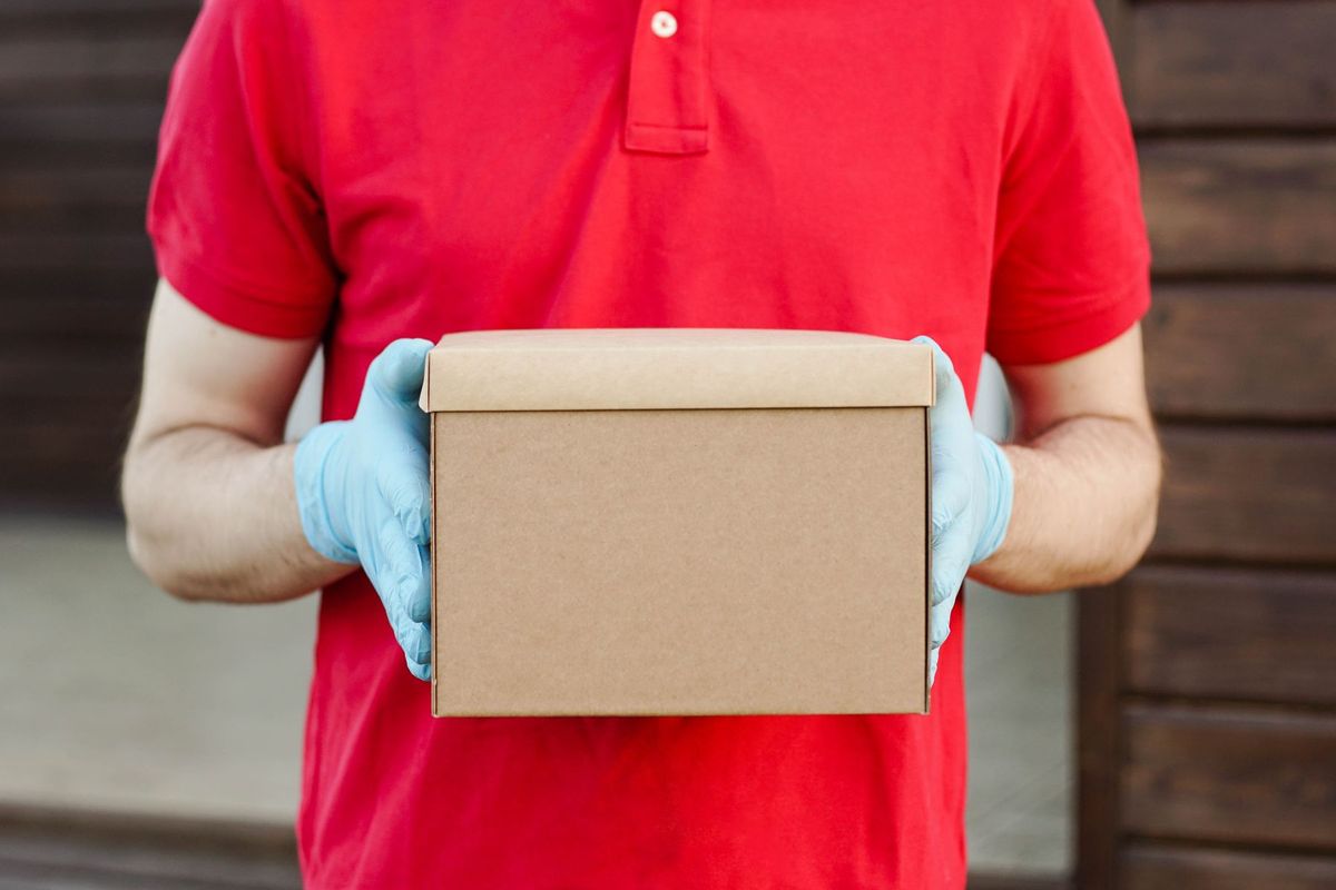 A delivery person in a red polo shirt and gloves holds a cardboard box, ready for delivery
