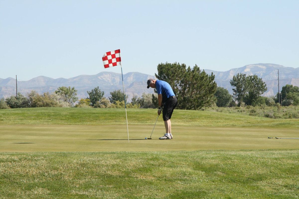 A golfer putting on a golf course under clear skies