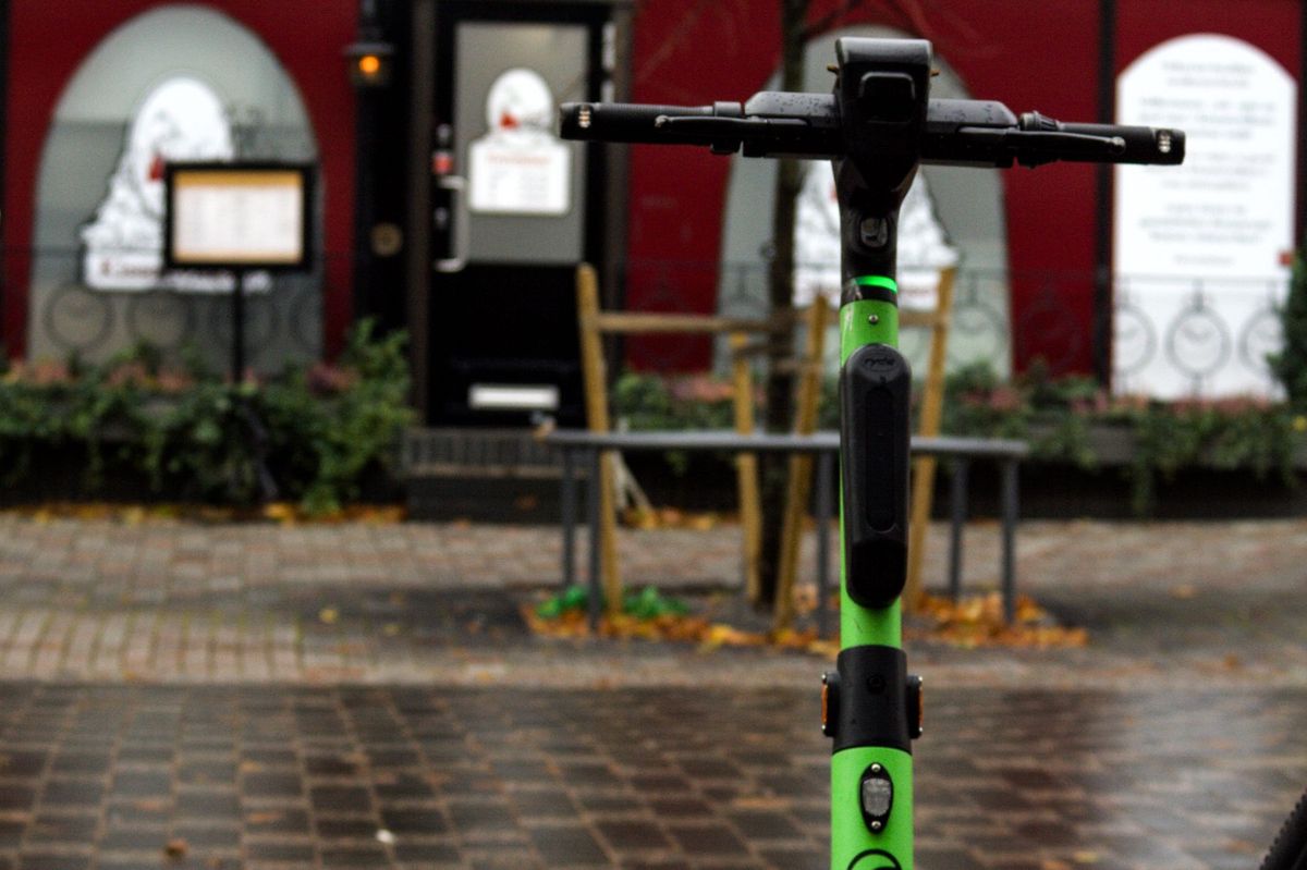 A green electric scooter strategically parked on a city sidewalk near a red storefront