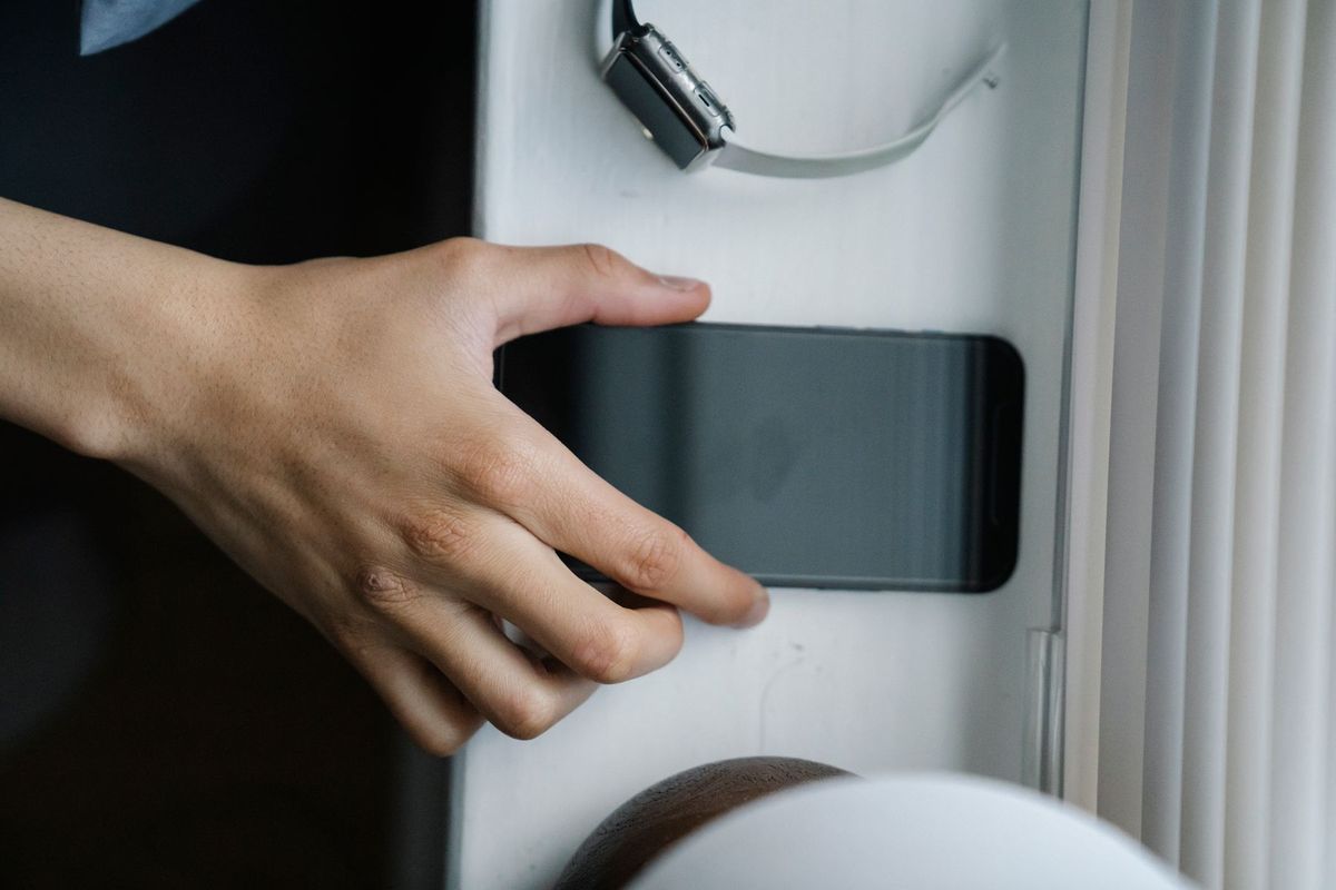 A hand reaches for a smartphone placed on a windowsill beside a wristwatch indoors