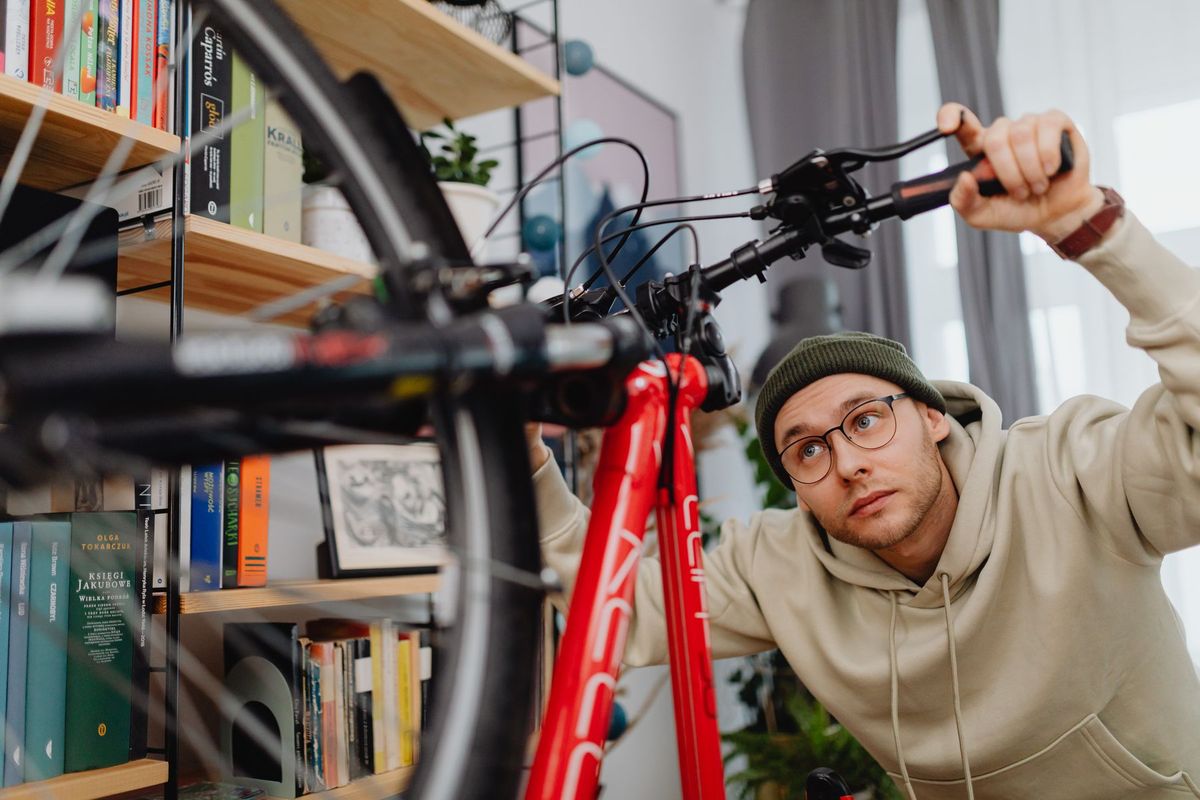 A man focuses on repairing a bicycle indoors, surrounded by bookshelves and tools