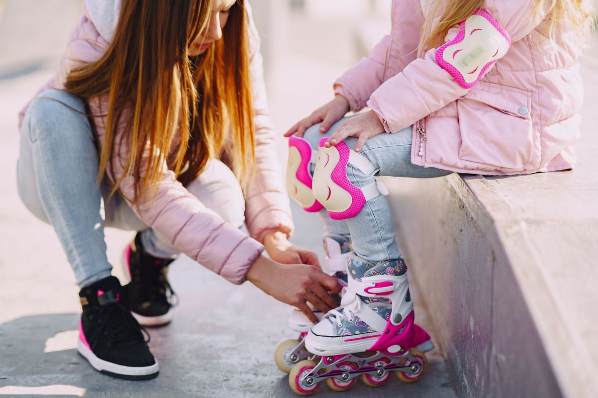 A mother assists her daughter with roller skates in a sunny urban setting