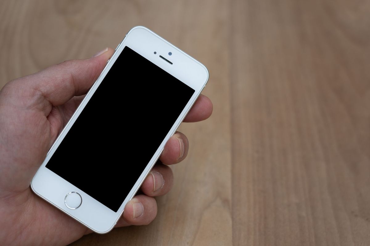 A person holding a smartphone with a blank screen over a wooden surface. Great for mockup use