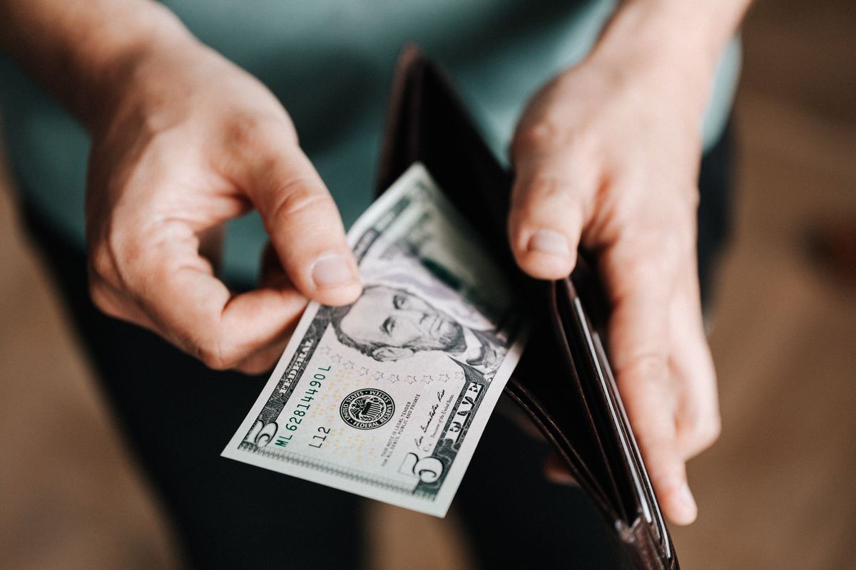 A person taking a five dollar bill from a wallet symbolizing personal finance and budget management