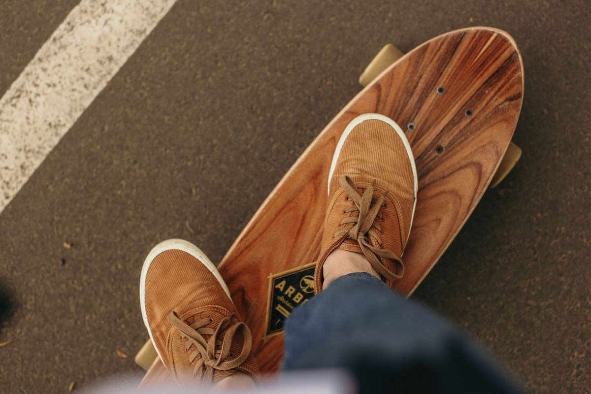 A person wearing brown sneakers balances on a wooden longboard, captured from above